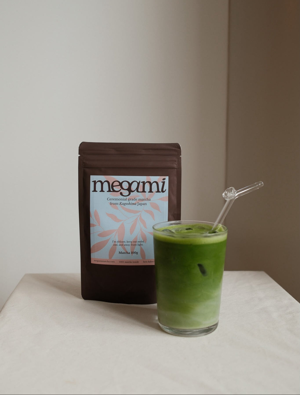 Iced matcha latte with a glass straw next to a pouch of Megami ceremonial matcha